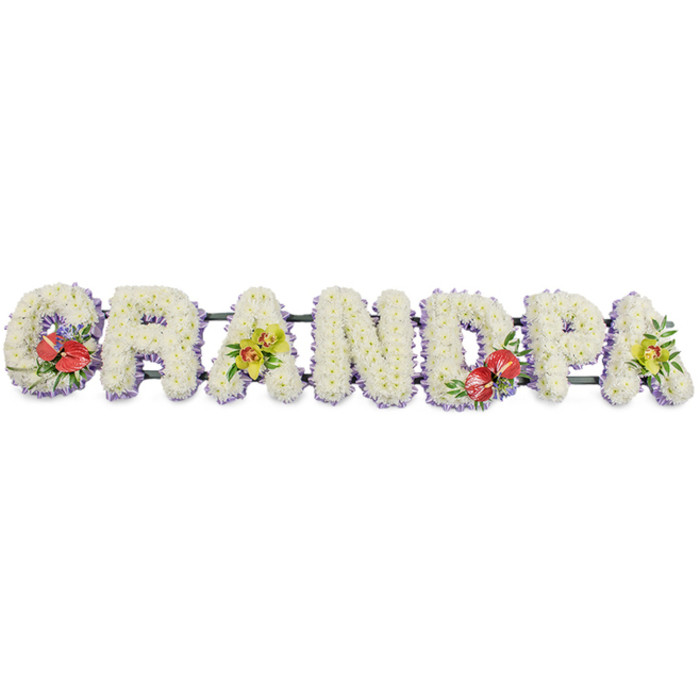 Set against a bright white background, a beautifully crafted funeral tribute spells out "GRANDPA" in large, three-dimensional block capitals, each letter made from compact clusters of white chrysanthemum heads that sit closely together like a soft floral tapestry. The chrysanthemums are immaculate and uniform, giving the word a clean, peaceful feeling as it stretches horizontally along a concealed, dark green metal frame that subtly anchors the design. At the base of every letter runs a trim of pale lavender ribbon, the soft purple hue peeping out just enough to define each outline and add a gentle, almost spiritual touch of colour. Carefully placed sprays of accent flowers interrupt the white in a thoughtful rhythm. On the "G" and the "D," bold red anthuriums with their smooth, waxy, heart-shaped petals and upright yellow centres rest among polished green leaves, bringing depth and a sense of steadfast love. On the first and final "A," clusters of yellow-green orchids, perhaps cymbidiums, with their graceful petals and fresh foliage, curve lightly across the chrysanthemums, hinting at warmth and treasured stories shared over the years. The arrangement feels composed for a Cowley family wanting a personalised floral name tribute delivered to a nearby chapel or crematorium, perhaps after a final visit at home. It is the sort of piece that would sit near a coffin or memory table, spelling out the affectionate title everyone used, while the white flowers and muted tones offer comfort and a respectful farewell to a much-loved grandfather.