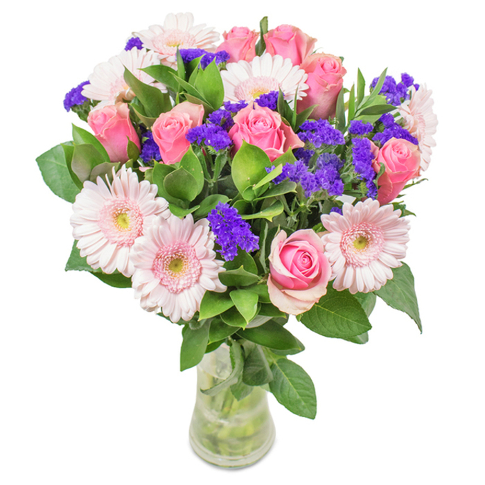 An elegant and vibrant floral display by Cowley Florist, this bouquet features approximately seven to nine lush, soft pink roses at varying stages of bloom-some tightly wrapped, others beginning to open, displaying the classic rose spiral. Interlaced are about five to seven pale pink gerbera daisies, each with a large, rounded face and lightly ruffled petals, their centers glimmering almost white beneath the soft overhead light. Vivid, purple statice-providing both textural contrast and deeper color-pop against the gentle hues, their dainty clusters filling the gaps with sprightly abundance. Lush, emerald green foliage serves as a foundation, cascading around the edges and reinforcing a sense of wild freshness, reminiscent of Cowley's leafy avenues and local gardens. The arrangement sits in a crystal-clear glass vase, stems and fresh water visible, grounding the bouquet in a natural, wholesome aesthetic. Tailored for occasions like birthdays, anniversaries, or spontaneous gestures of affection, this bouquet encapsulates the spirit of celebration and heartfelt connection and is available for same-day delivery throughout Cowley and nearby communities.